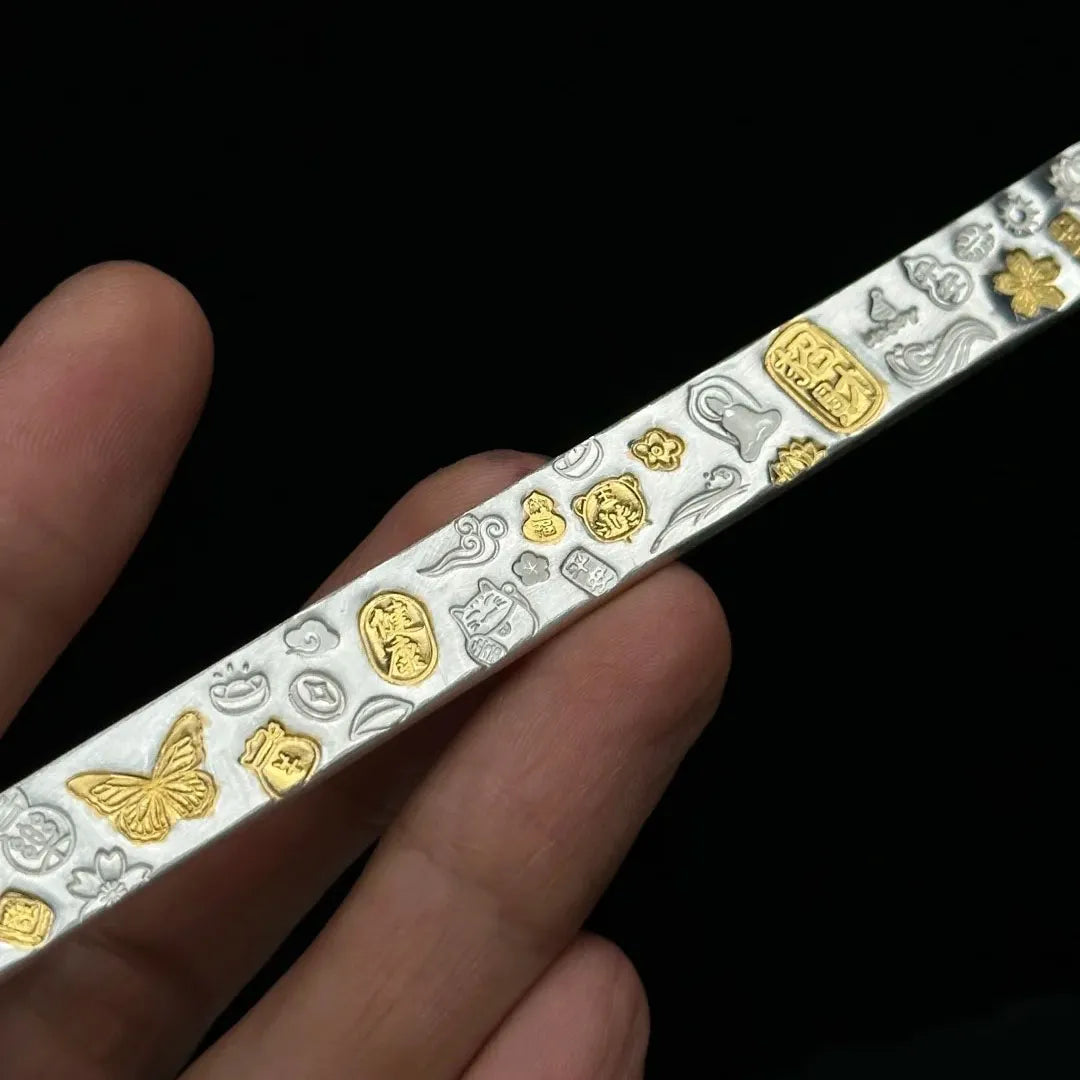 Decorative belt with gold and silver patterns held by a hand against a black background