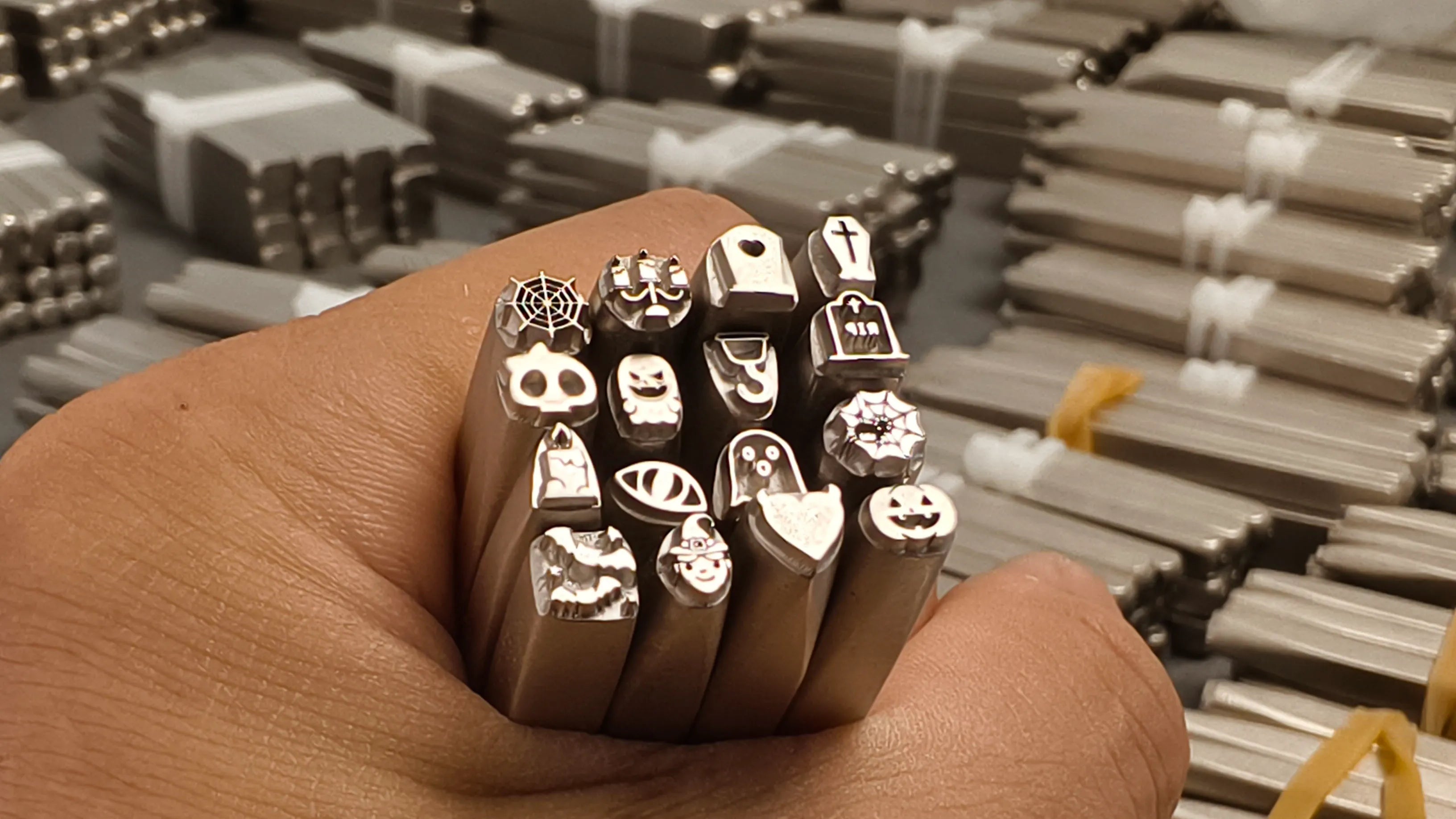 Metal stamps held in a hand with metal products in the background