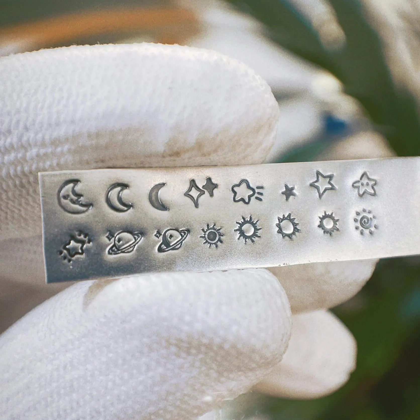 Metal stamping block with various celestial designs held by a gloved hand.