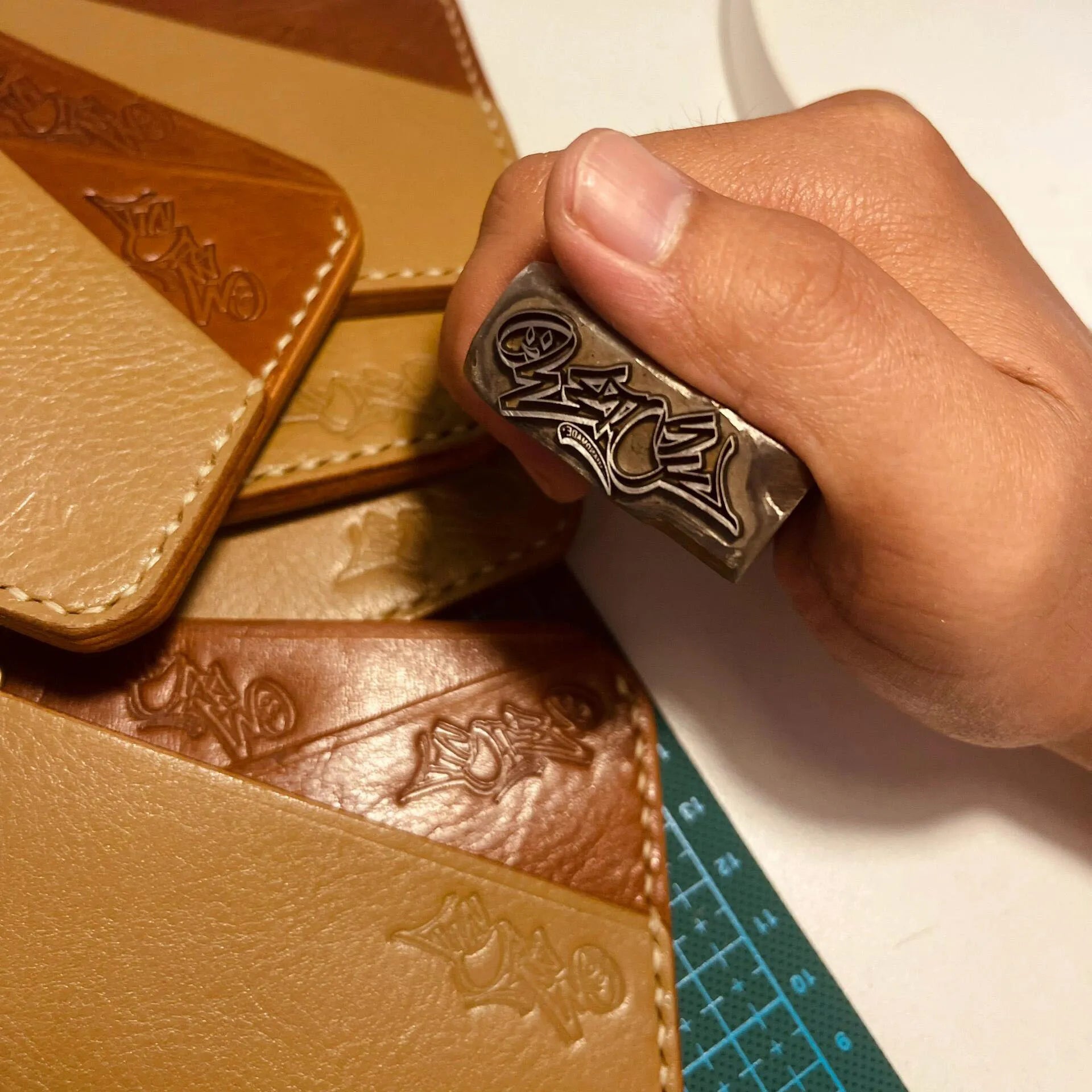 Hand stamping brown leather with a decorative tool on a white surface.